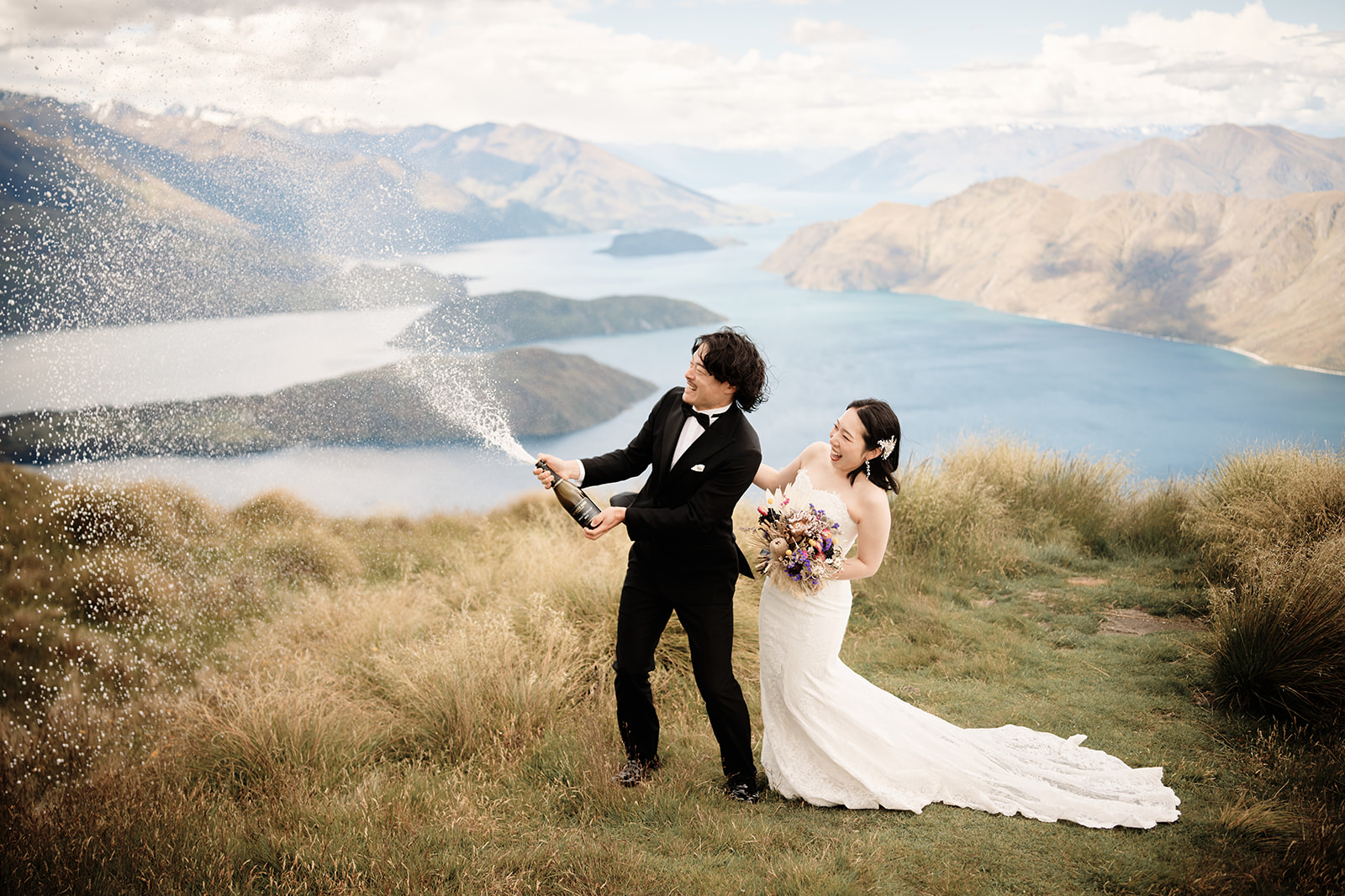 Queenstown Wedding Photographer A bride and groom celebrating their 結婚式 by spraying champagne on top of a mountain in クイーンズタウン, ニュージーラ